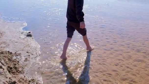 Child boy walks on shallow water in river with sand bottom barefooted legs. — 비디오