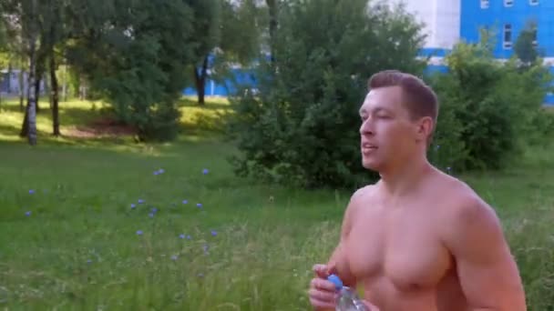 Jonge sporter jogt in stadspark met naakt bovenlijf en drinkwater. — Stockvideo