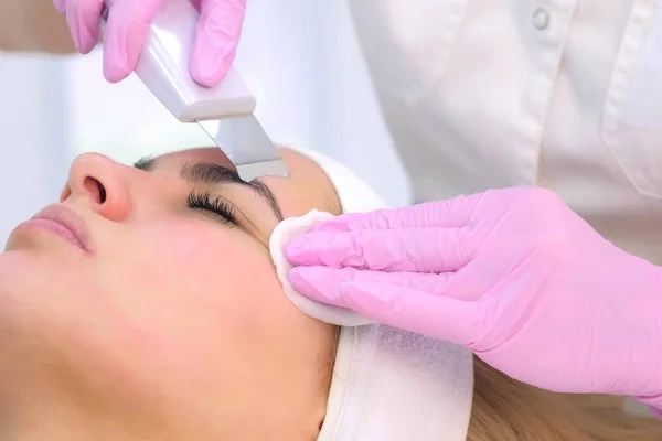 Cosmetoloog maakt ultrasone gezichtsreiniging procedure om jonge vrouw in kliniek. — Stockfoto