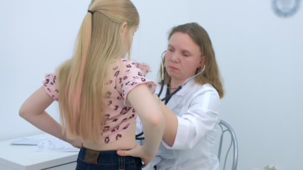 Mujer pediatra escuchando el latido del corazón de una niña usando estetoscopio en la clínica . — Vídeos de Stock