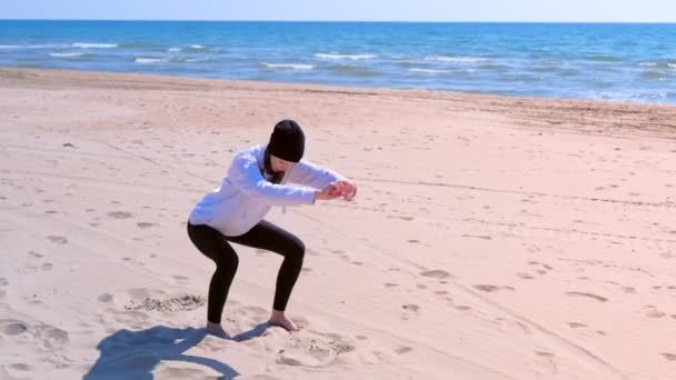 Mujer hace sentadillas en la playa de arena de mar fitness ejercicios deportivos al aire libre en el entrenamiento . — Vídeos de Stock