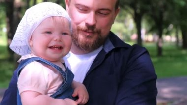 Şehir parkında kızını kucağında tutan genç bir baba, kameraya bakan aile fotoğrafı..