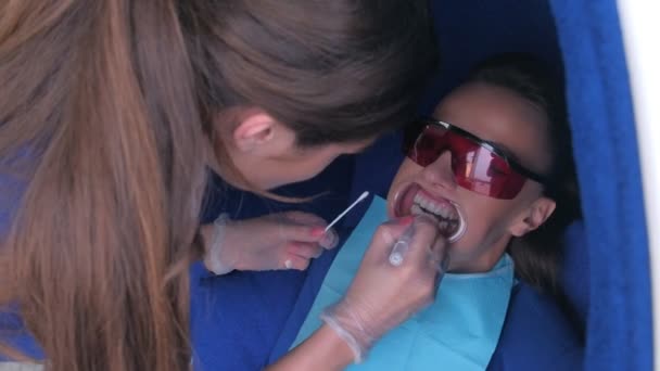 Nurse applying gel for LED whitening on woman patients teeth in dentistry. — Stockvideo