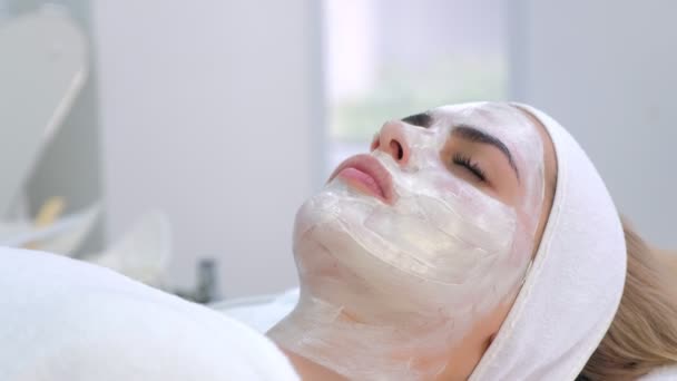 Frauenporträt im Wellness-Salon mit weißer Maske im Gesicht, Ansicht von unten. — Stockvideo