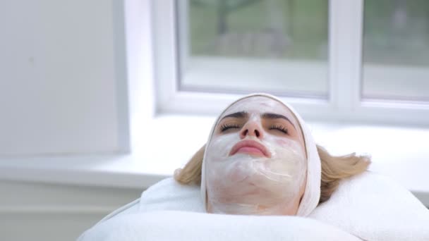 Frauenporträt im Wellness-Salon mit weißer Maske im Gesicht, Ansicht von unten. — Stockvideo