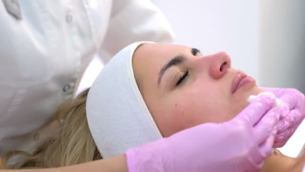 Cosmetologist em luvas limpando máscara de cara de mulher jovem, vista lateral . — Vídeo de Stock