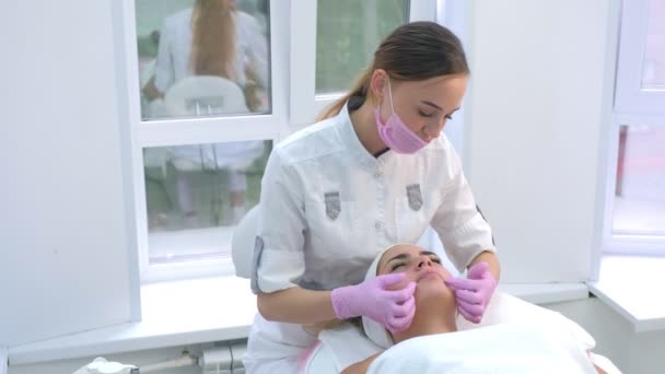 Cosmetoloog aanbrengen crème op klanten vrouw gezicht en nek en masseren. — Stockvideo