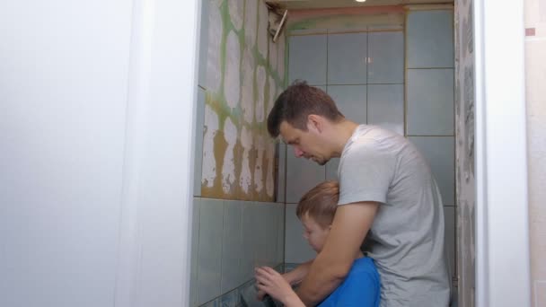 Vater und Sohn renovieren gemeinsam zu Hause, entfernen Fliesen von Wänden in der Toilette. — Stockvideo