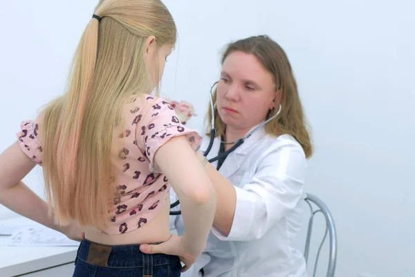 Pediatrician woman listening to heartbeat of girl using stethoscope in clinic.