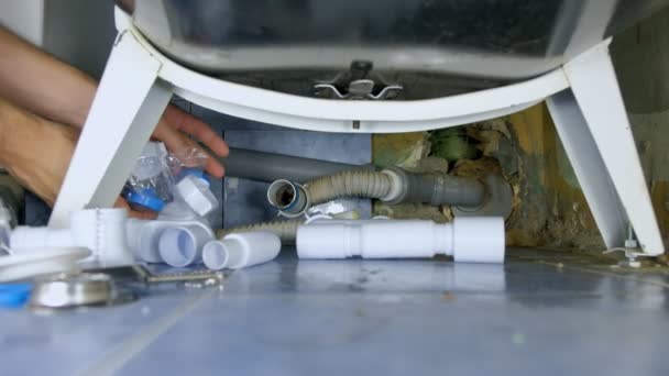 Plumber repairs replacement of pipes with new ones under bath in bathroom. — 비디오