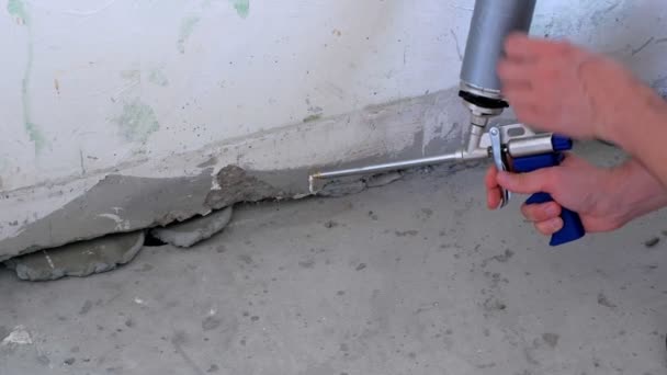 Obrero llena grieta entre la pared y el suelo de cemento con espuma de montaje en la habitación . — Vídeos de Stock