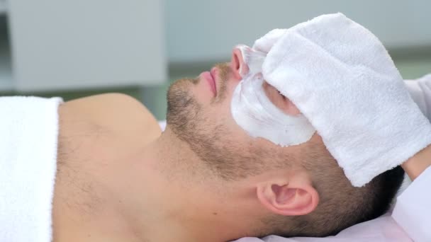 Cosmetoloog veegt hydraterende masker van mannen gezicht met behulp van badstof wanten. — Stockvideo