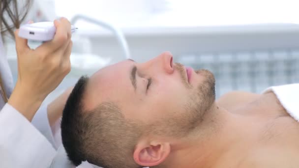 Kosmetolog wykonuje ultradźwiękowy zabieg oczyszczania twarzy u młodego mężczyzny w klinice. — Wideo stockowe