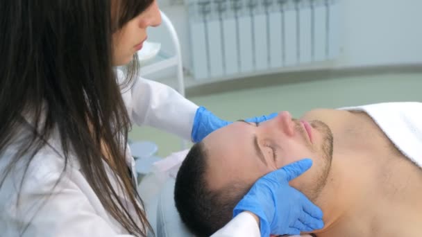 Kosmetikerin mit Handschuhen cremt Kunden ein Mann massiert Haut im Gesicht. — Stockvideo