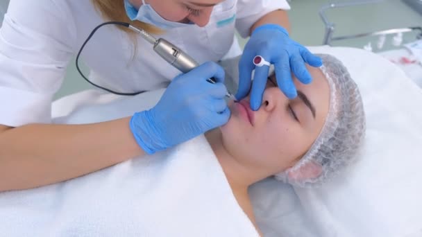 Esteticista aplicando maquillaje permanente en labios de mujer dibujo usando máquina de tatuaje. — Vídeos de Stock