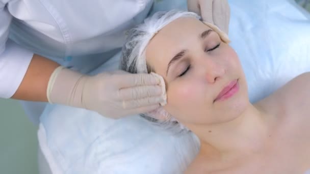 Cosmetologist limpa o rosto das mulheres com almofadas de algodão na clínica de beleza, close-up. — Vídeo de Stock