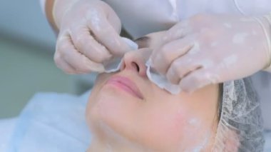 Kozmetik uzmanı, güzellik kliniğinde pamuk pedlerle kadınların yüzlerindeki maskeyi siliyor..