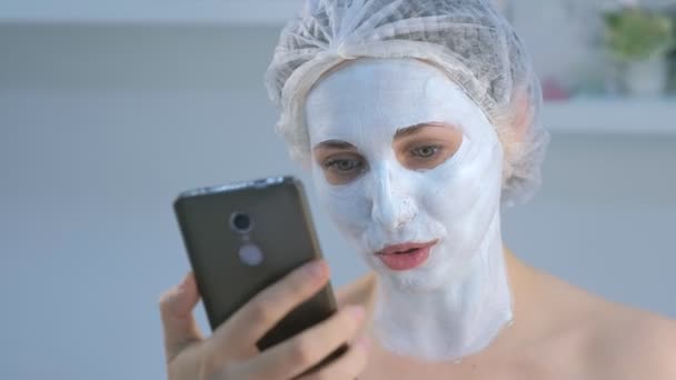 Vrouw blogger maken selfie met gezichtsmasker op mobiele telefoon in schoonheid kliniek. — Stockvideo