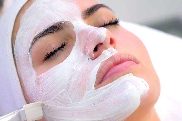 Cosmetólogo está aplicando máscara blanca en cara de cliente mujer en clínica de belleza . — Foto de Stock