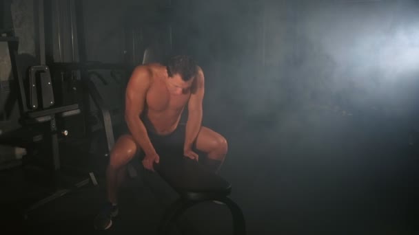 Втомився молодий чоловік культурист лежить на лавці відпочиває в спортзалі після тренувань . — стокове відео