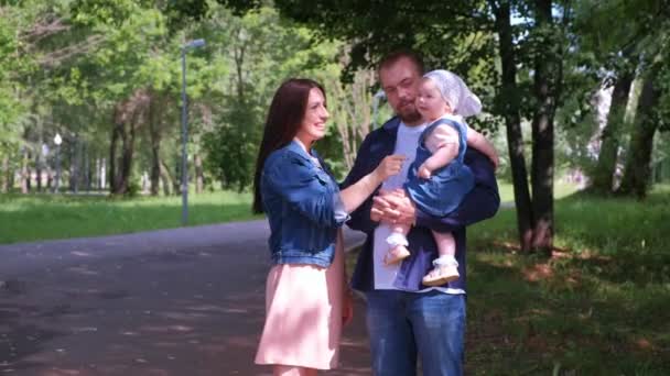 Retrato familiar en el parque de la ciudad con mamá, papá e hija bebé mirando a la cámara . — Vídeo de stock