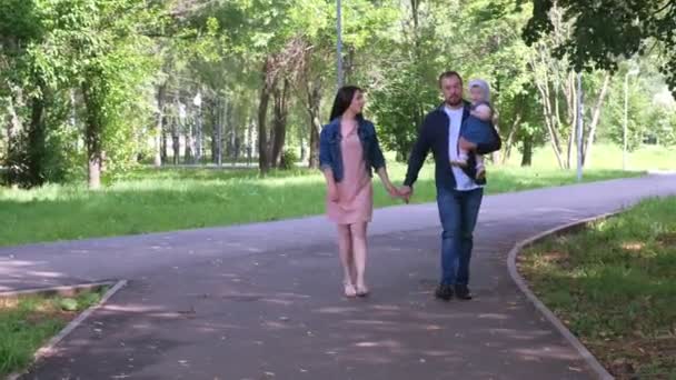 Retrato familiar caminando en el parque de la ciudad con mamá, papá e hija bebé en las manos . — Vídeo de stock