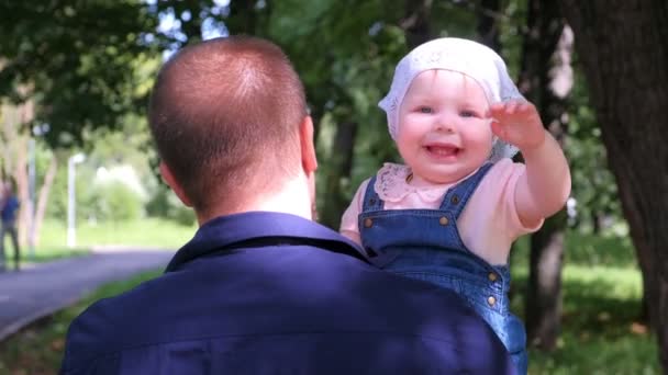 Mladý táta drží dceru v městském parku, rodina, dítě dívá do kamery. — Stock video