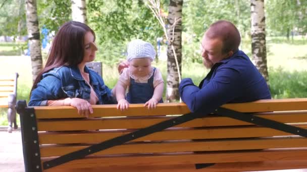 Familj mamma och pappa sitter och leker på bänk i stadsparken med lilla flickan. — Stockvideo