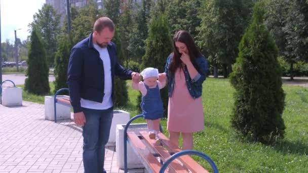 Papa en mama houden elkaars hand vast baby meisje gaat 's zomers langs de bank in het park. — Stockvideo