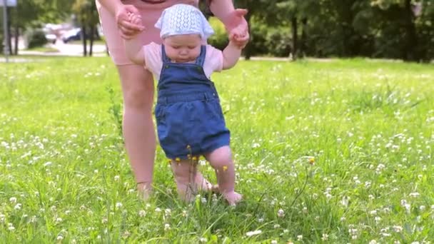 Moeder leren baby meisje om te lopen, eerste stappen in het park met blootsvoets benen. — Stockvideo