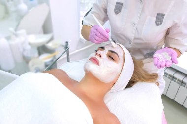 Kozmetik uzmanı, güzellik kliniğinde kadın müşteri yüzüne beyaz maske takıyor..