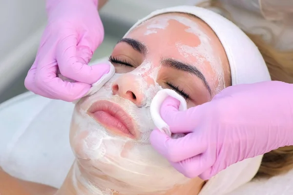 Cosmetoloog in handschoenen veegt masker van vrouwen gezicht, close-up portret. — Stockfoto