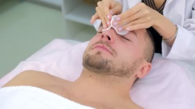Man on cleaning face procedure by woman cosmetologist in beauty clinic.