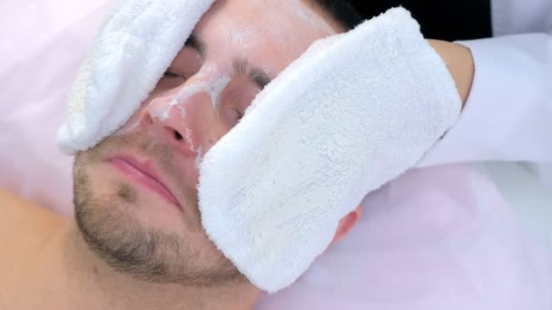 Cosmetoloog veegt hydraterende masker van mannen gezicht met behulp van badstof wanten. — Stockvideo