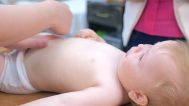 Doctor massagist making massage to baby on tummy in clinic lying on couch.