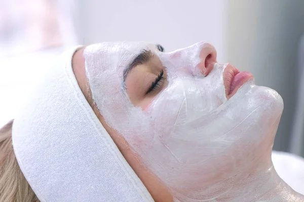 Portrait of woman laying in spa salon with white mask on face, side view. — Stockfoto