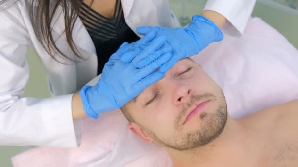 Cosmetoloog in handschoenen is het aanbrengen van crème op klanten man gezicht masseren huid. — Stockvideo