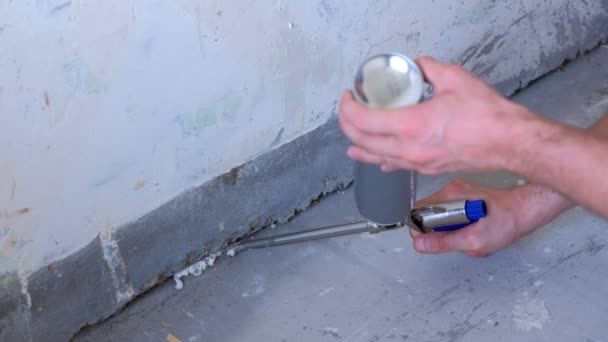 Arbeiter füllt Riss zwischen Wand und Zementboden mit Schaumstoff im Raum. — Stockvideo