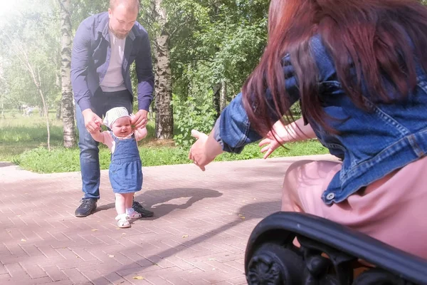 Mamá y papá enseñando a la niña a caminar los primeros pasos tomados de la mano . —  Fotos de Stock