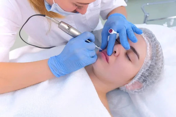 Esteticista aplicando maquiagem permanente em desenho de lábios de mulher usando máquina de tatuagem. — Fotografia de Stock