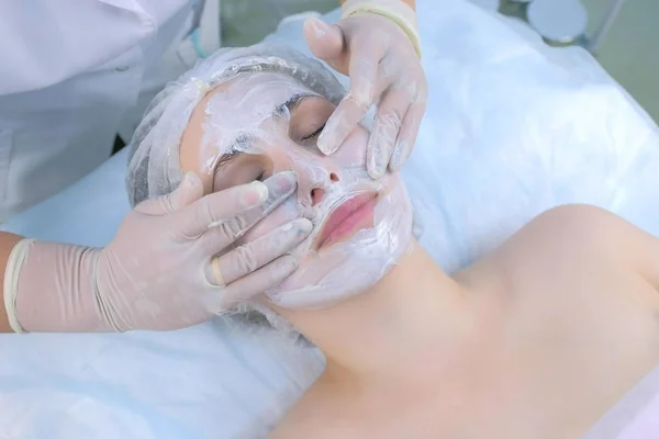 Beautician is applying facial moisturizing mask on woman face in beauty clinic.
