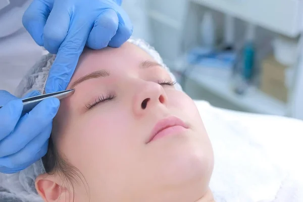 Esteticista arranca o cabelo em sobrancelhas com pinças de mulher, close-up de cara. — Fotografia de Stock