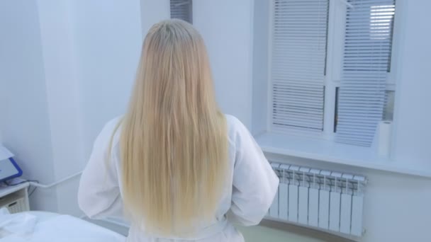 La donna che si prepara a massaggiare togliendosi l'accappatoio si siede sul divano in clinica, vista posteriore . — Video Stock