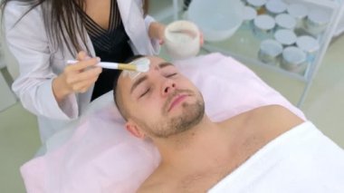 Kozmetik uzmanı beyaz nemlendirici maskeyi erkeklerin yüzüne fırça kullanarak uyguluyor..
