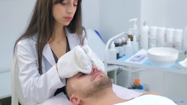 Cosmetoloog veegt hydraterende masker van mannen gezicht met behulp van badstof wanten. — Stockvideo