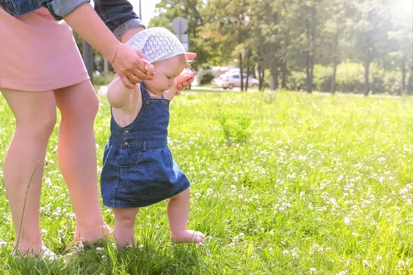 Mama uczy dziewczynkę chodzić, pierwsze kroki w parku boso nogi, widok z boku. — Zdjęcie stockowe