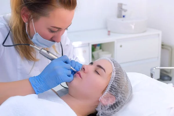 Cosmetologist que faz o procedimento microblading dos lábios para a menina que usa a máquina da tatuagem. — Fotografia de Stock