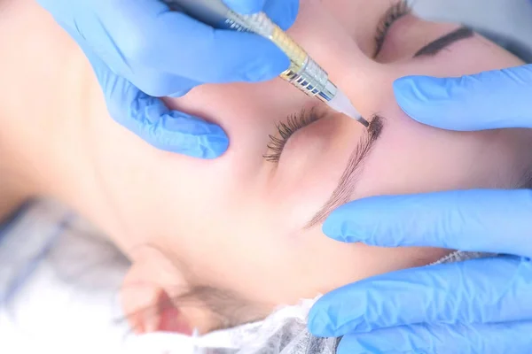 Beautician making eyebrows microblading procedure in beauty salon for woman.