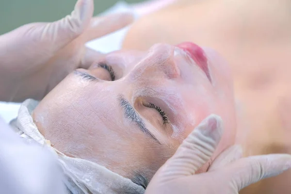 Kosmetolog gør ansigtsmassage med fugtgivende maske på kvinders ansigt . - Stock-foto