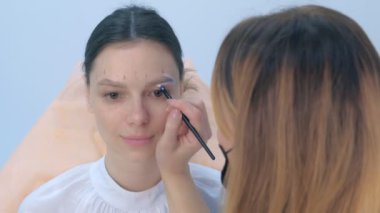 Cosmetologist painting brush shape of eyebrows woman before tint procedure.